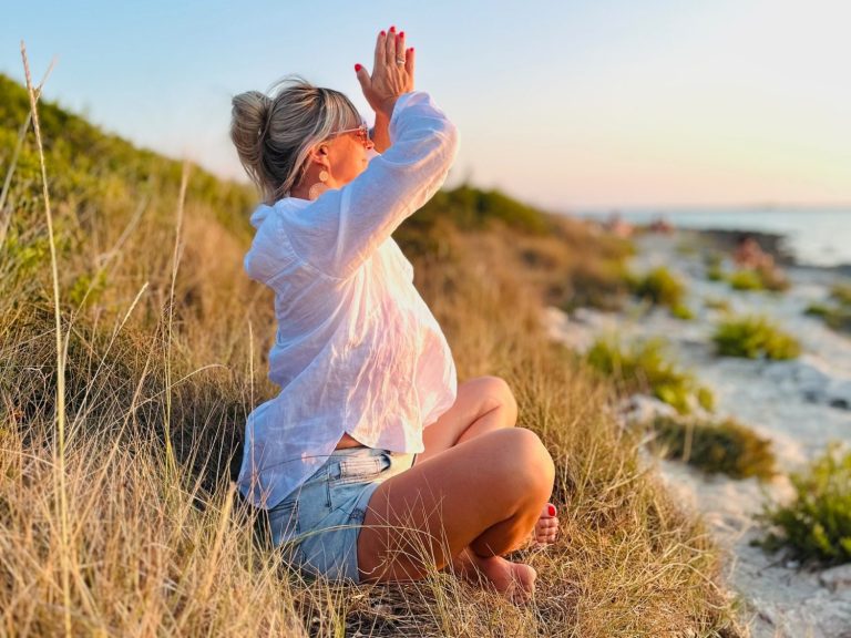 Frau in Sportkleidung macht eine Yoga-Übung am Meer unter blauem Himmel.
